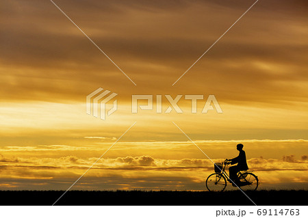 夕焼け 自転車 夕陽 土手 シルエット 影の写真素材