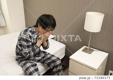 ベッドルームにてパジャマ姿でくしゃみをする男性