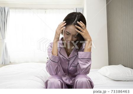 病気で寝込んでいる女性/体調の悪い女性/ベットに寝ている美しい女性/ベッドに座っている美人