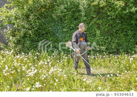 A Young White Man in a Straw Hat is Mowing a Lawn with a Lawn